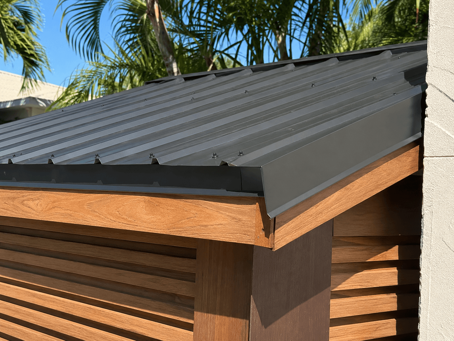 Dark corrugated metal roof over cedar horizontal slats on custom water system cover by Benito Fine Carpentry Palm Beach County