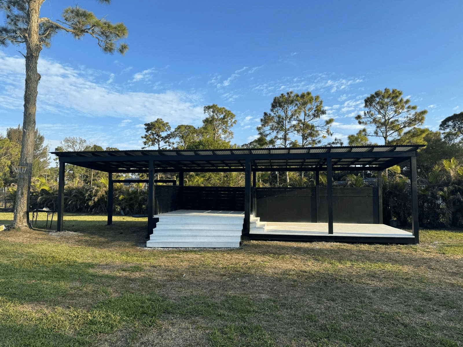 Modern black outdoor pavilion with corrugated metal roof and white deck built by Benito Fine Carpentry Wellington FL